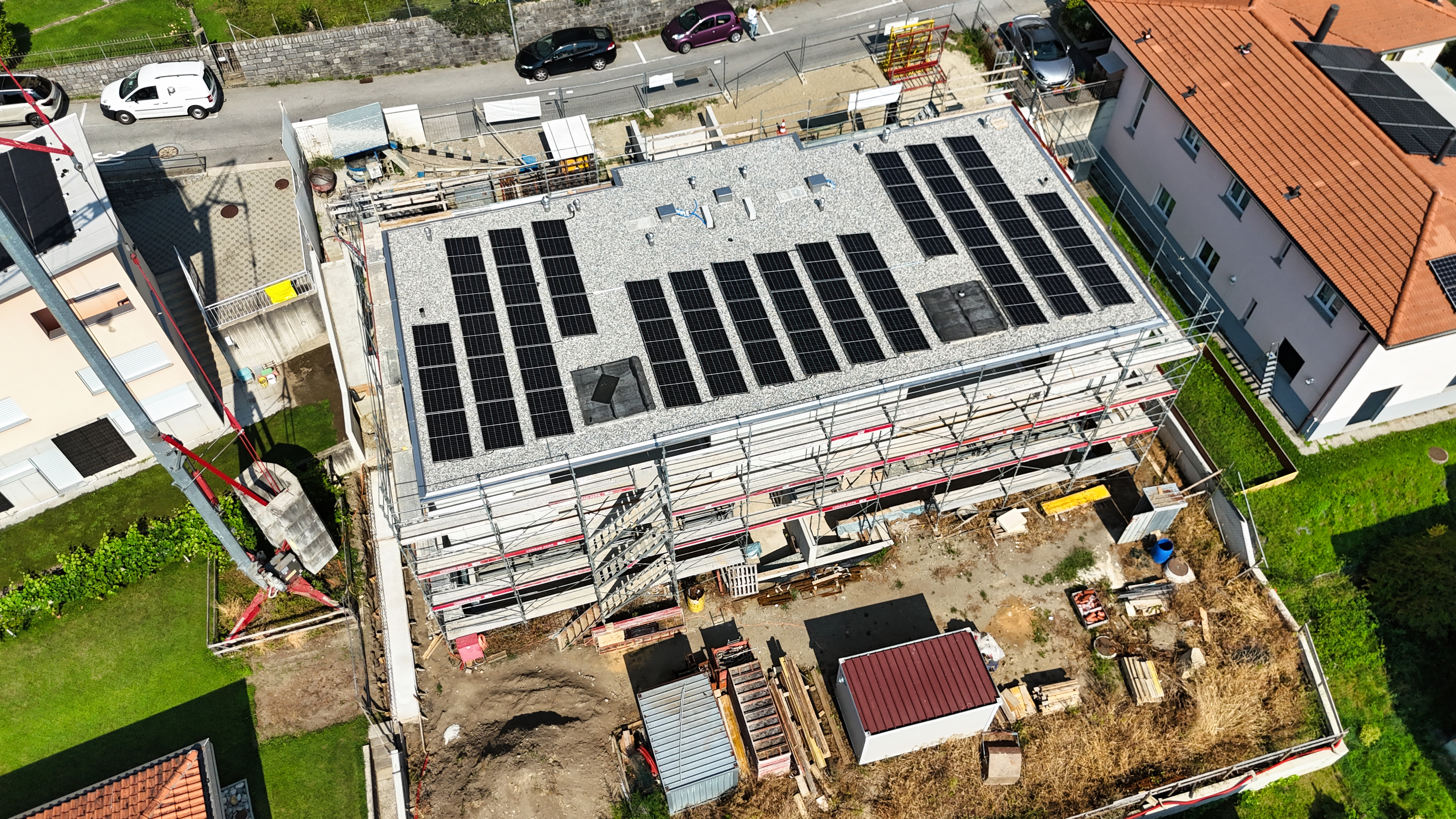An aerial view of a building under construction, predominantly made of concrete and featuring solar panels on its partiall...